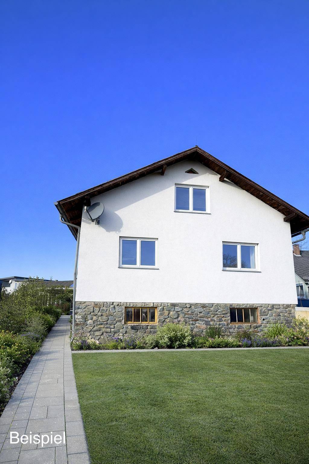 Weißes Einfamilienhaus mit Steinsockel, Satteldach und gepflegtem Vorgarten unter blauem Himmel.