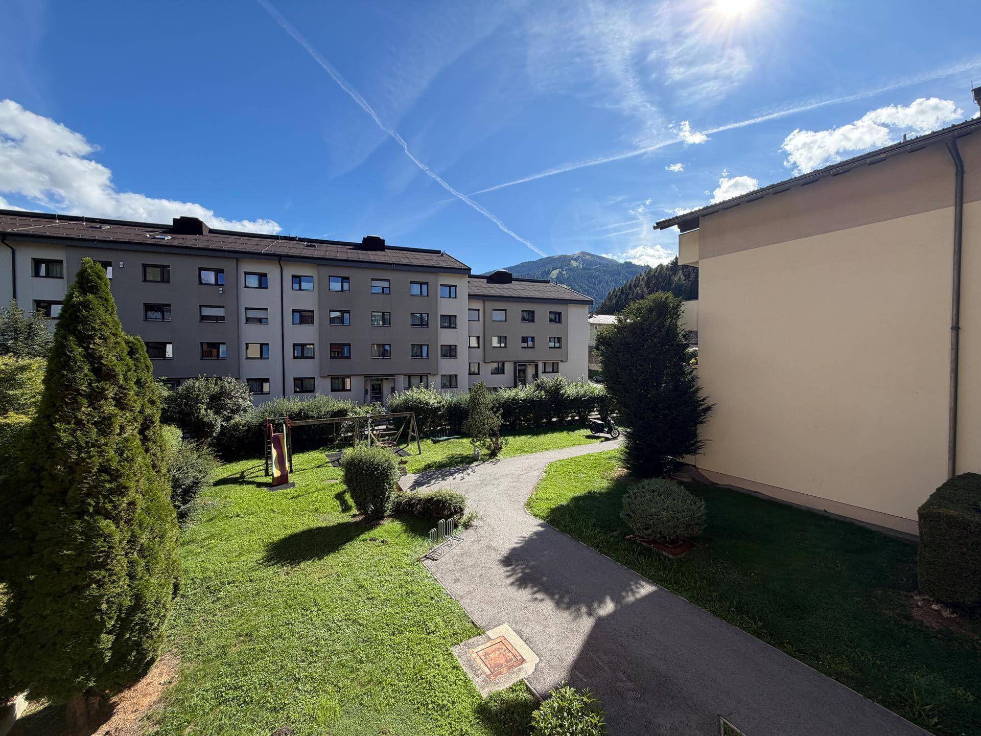 Außenansicht von Wohngebäuden mit einem grünen Innenhof, Spielplatz und Bergblick.