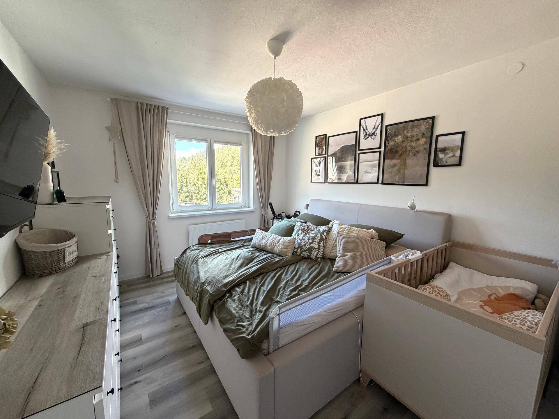 Schlafzimmer mit Doppelbett, Babybett und Kommode, hell und freundlich gestaltet.