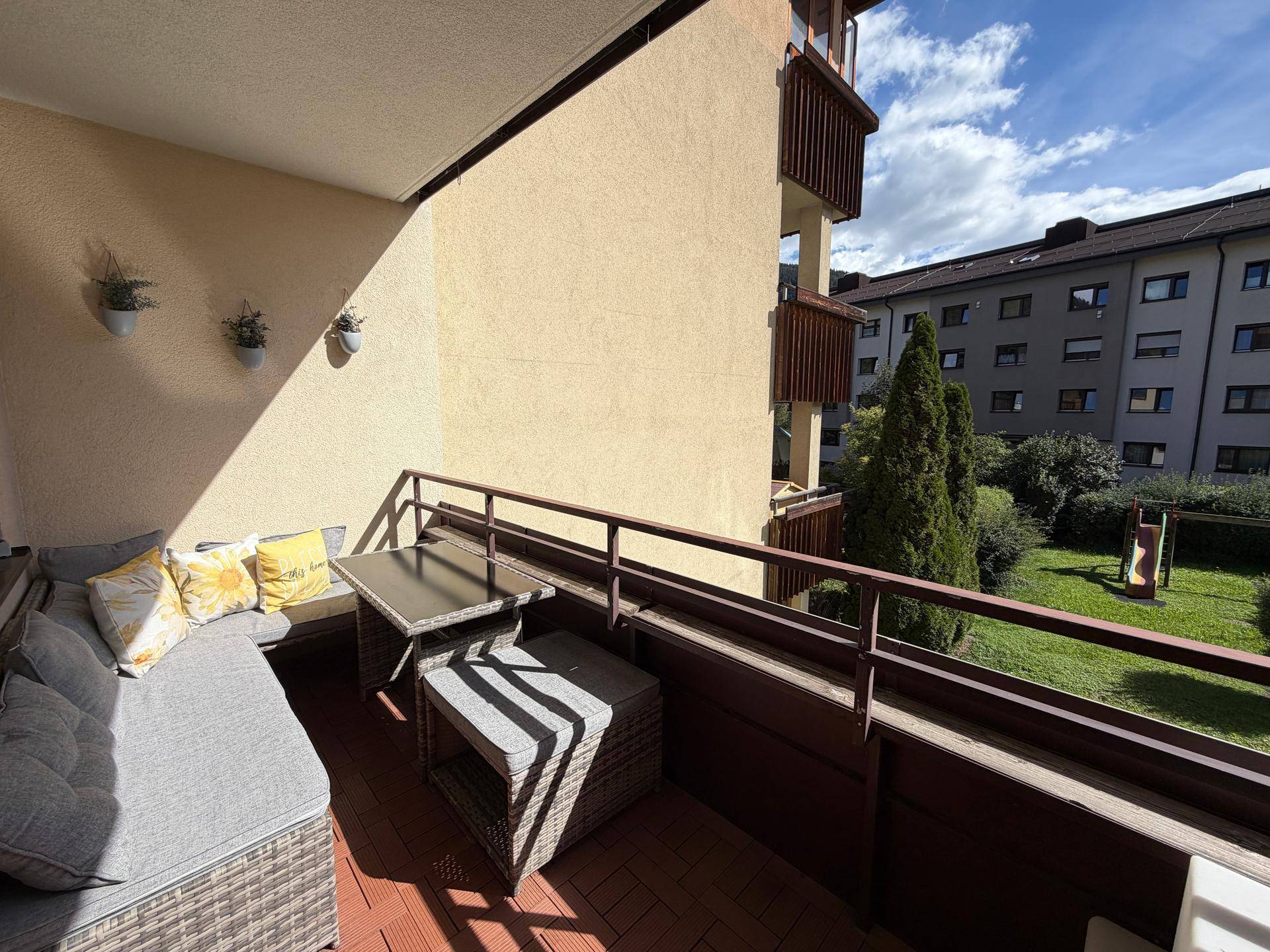 Gemütlicher Balkon mit Sitzgelegenheiten und Blick auf den grünen Innenhof mit Spielplatz.