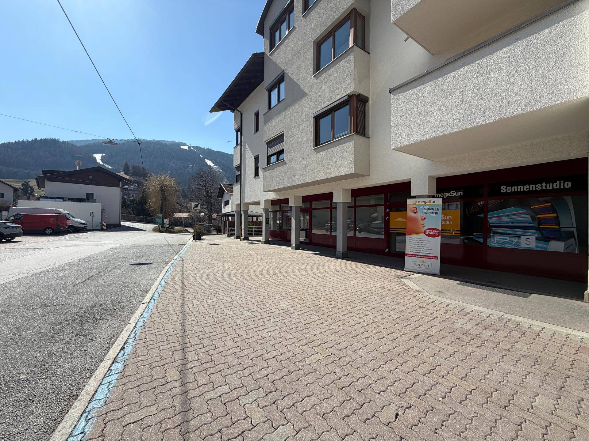 Außenansicht eines Geschäftsgebäudes mit gepflastertem Gehweg und Blick auf die umliegende Berglandschaft.