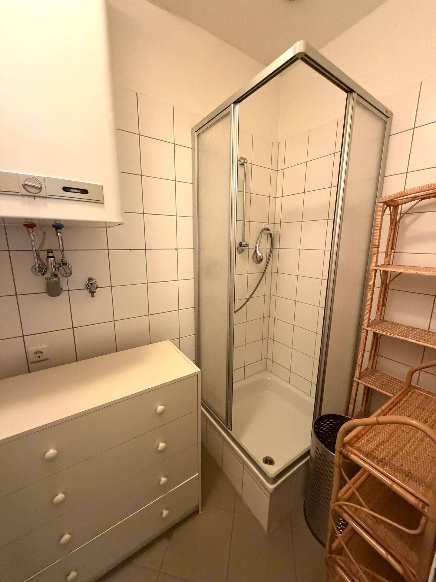 Kleines Badezimmer mit Duschkabine, weißen Fliesen und Warmwasserboiler.