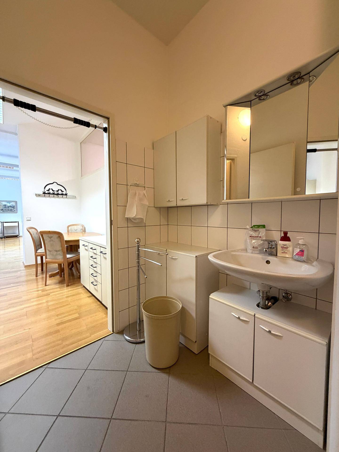 Badezimmer mit Fliesenboden, Waschbecken, Spiegelschrank und Platz für eine Waschmaschine.