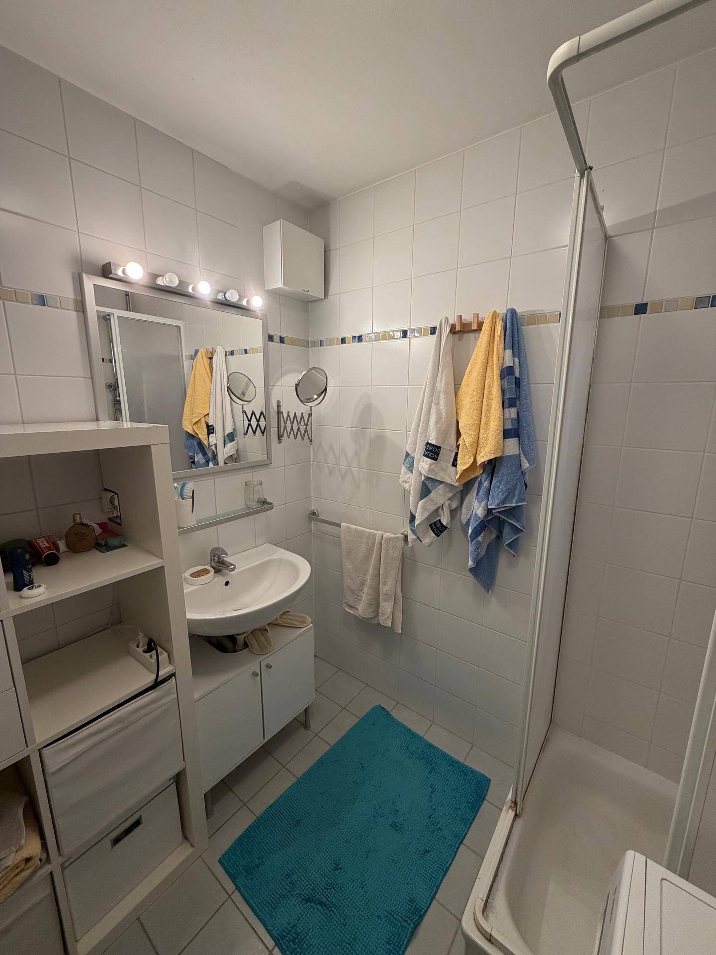 Gefliestes Badezimmer mit Waschbecken, Spiegel und einer Duschkabine, ausgestattet mit grundlegenden Armaturen.