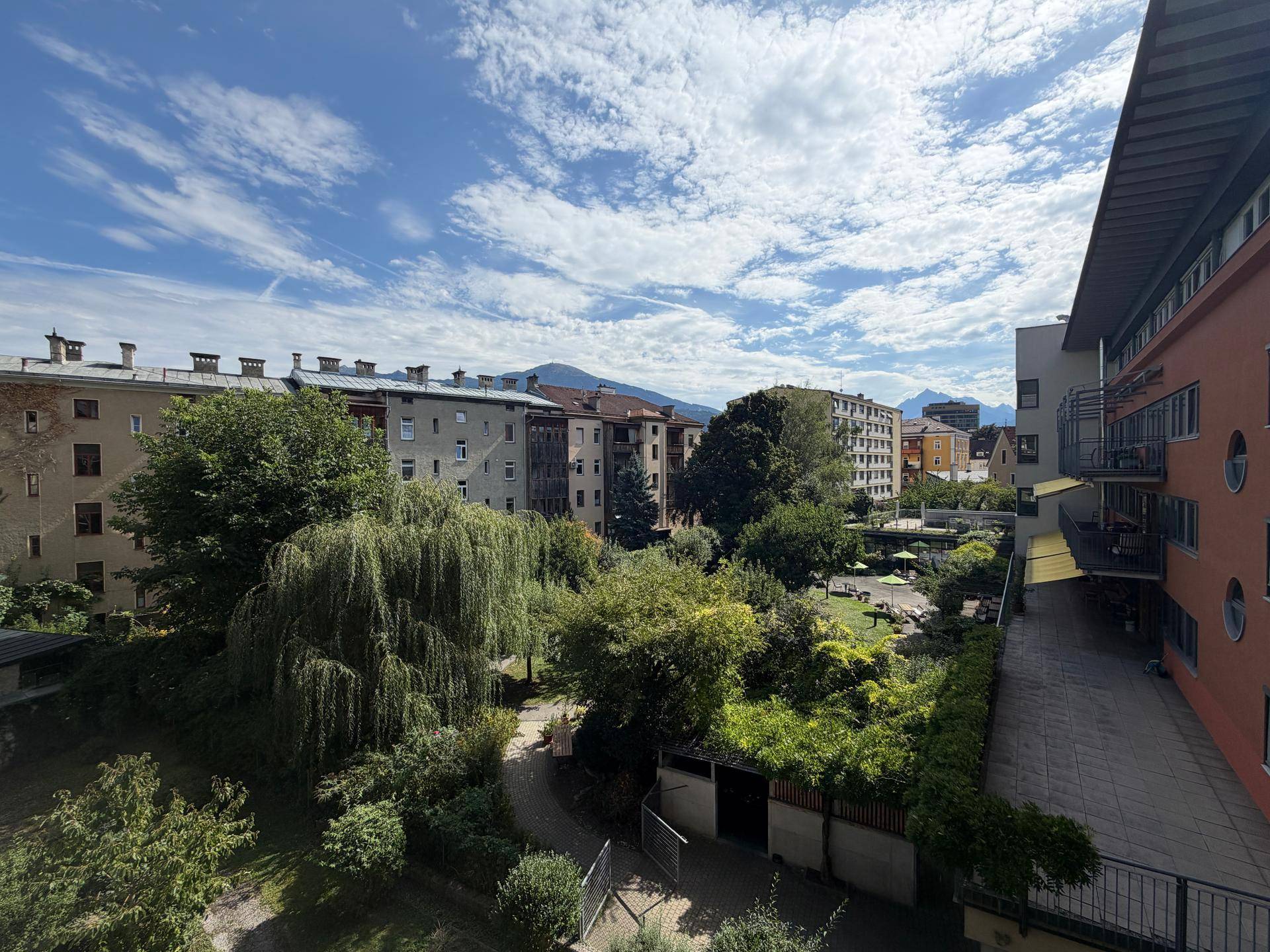 Weitläufiger Blick auf einen grünen Innenhof, umliegende Gebäude und die Berglandschaft im Hintergrund.