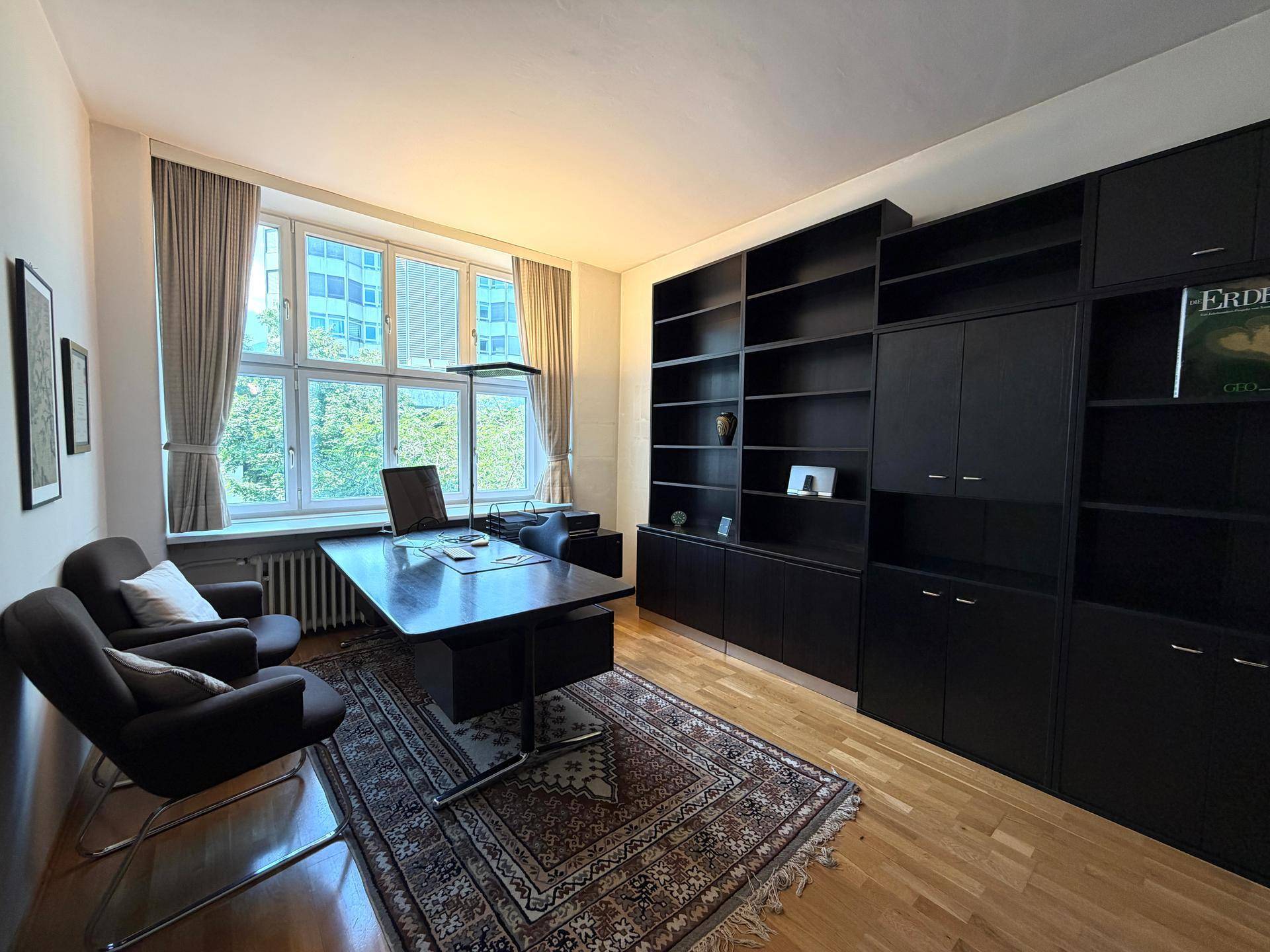 Elegantes Büro mit dunklem Schreibtisch, großen Bücherregalen und bequemen Sesseln am Fenster.