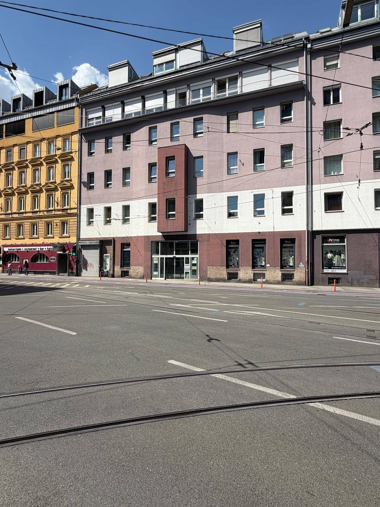 Mehrstöckiges Gebäude mit verschiedenen Fassadenfarben, gesehen von der gegenüberliegenden Straßenseite.