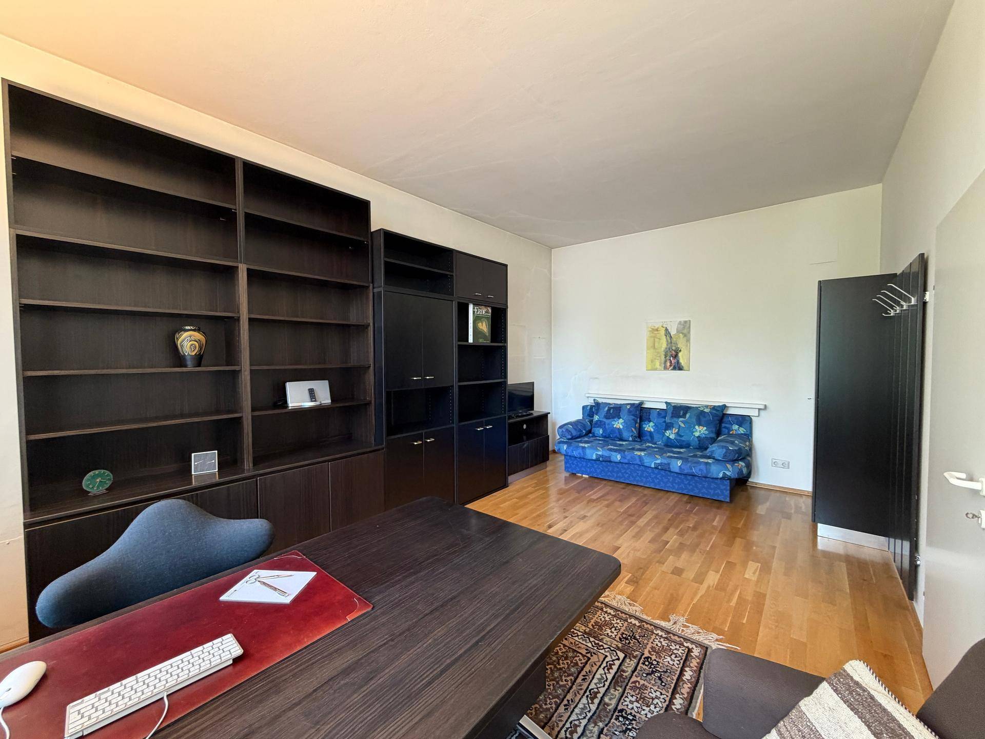 Kombinierter Büro- und Wohnbereich mit großem Schreibtisch, Bücherregalen und einem blauen Sofa.