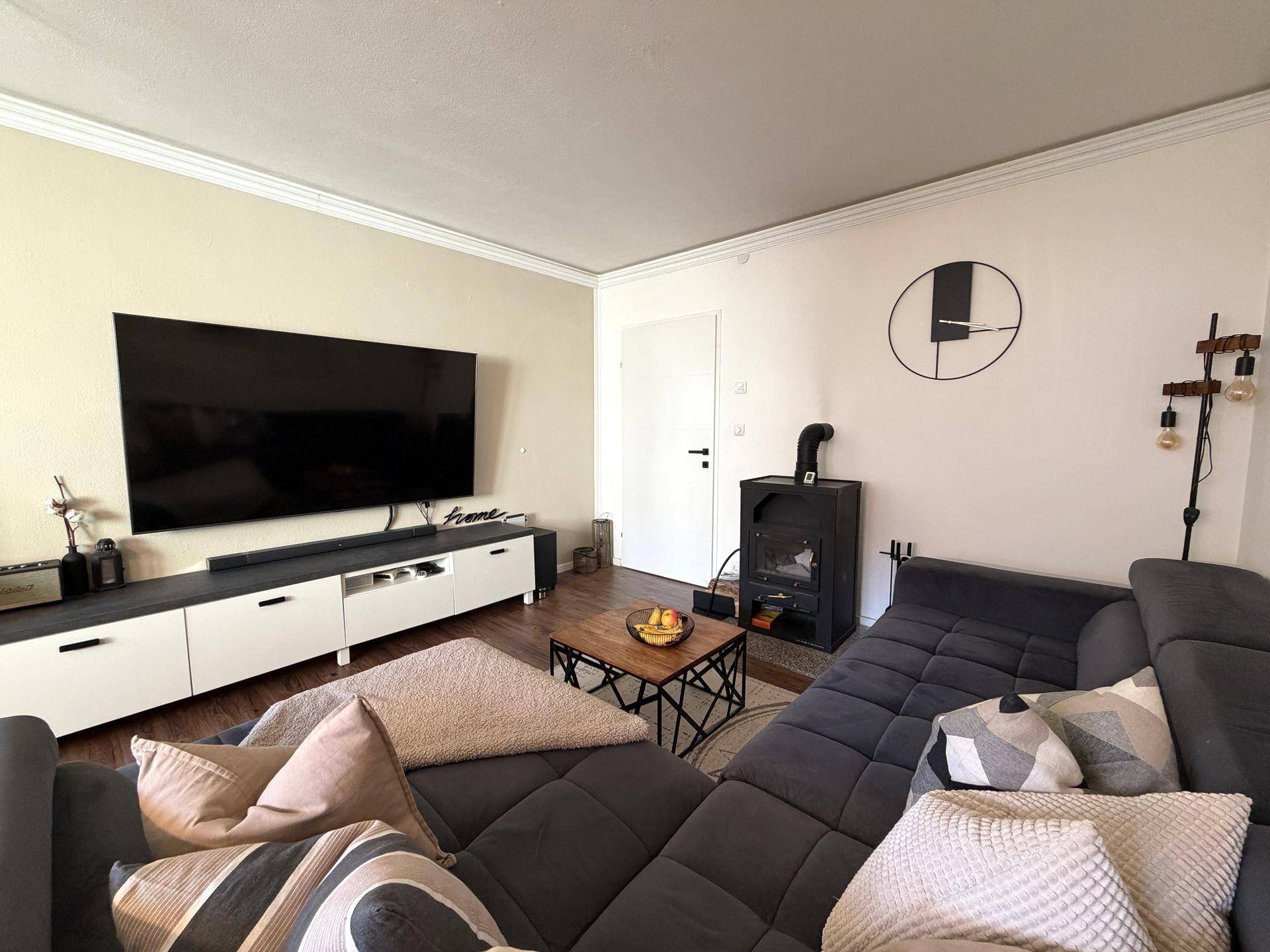 Gemütliches Wohnzimmer mit großem Fernseher, Sofa und einem Holzofen.