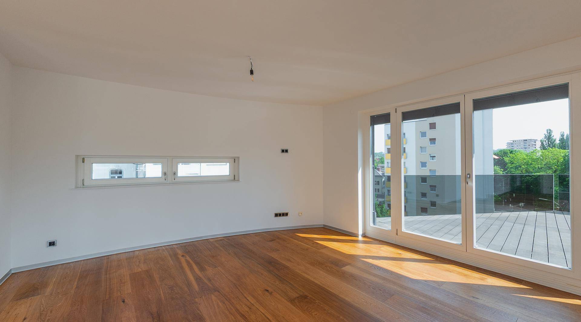 Geräumiger, heller Raum mit Holzboden und großen Fenstern mit Blick auf die Stadt.