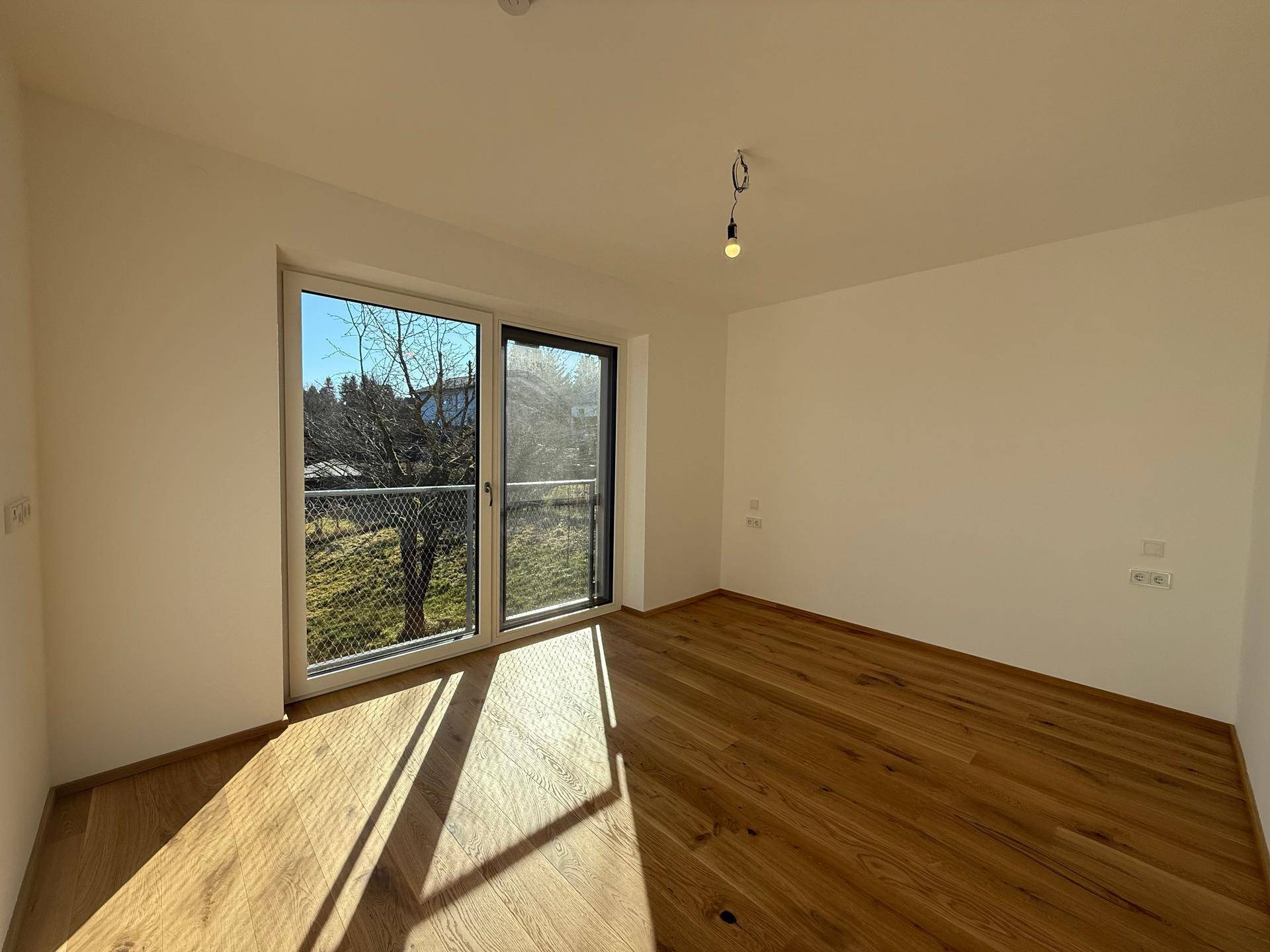 Helles Schlafzimmer mit Holzboden und großem Fenster mit Blick ins Grüne.
