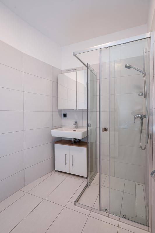 Modernes Badezimmer mit Duschkabine, Waschbecken und weißen Fliesen an Wänden und Boden.