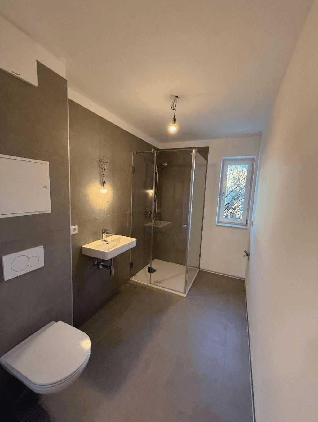 Modernes Badezimmer mit grauen Fliesen, bodengleicher Dusche und wandhängendem WC, hell und funktional.