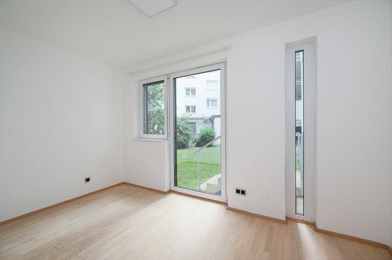 Heller Raum mit Parkettboden und Zugang zum Garten durch eine Glastür.