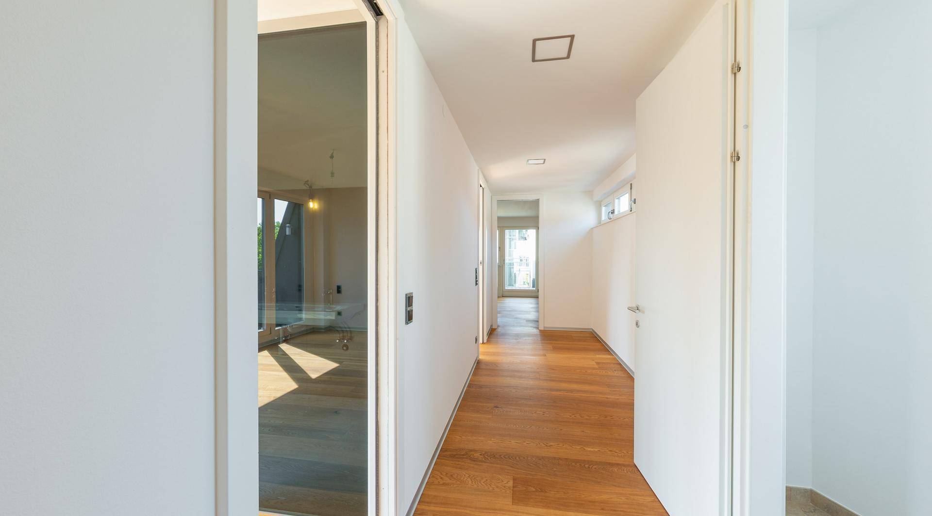 Heller Flur mit Holzboden und einer modernen Glastür, die zu weiteren Räumen führt.