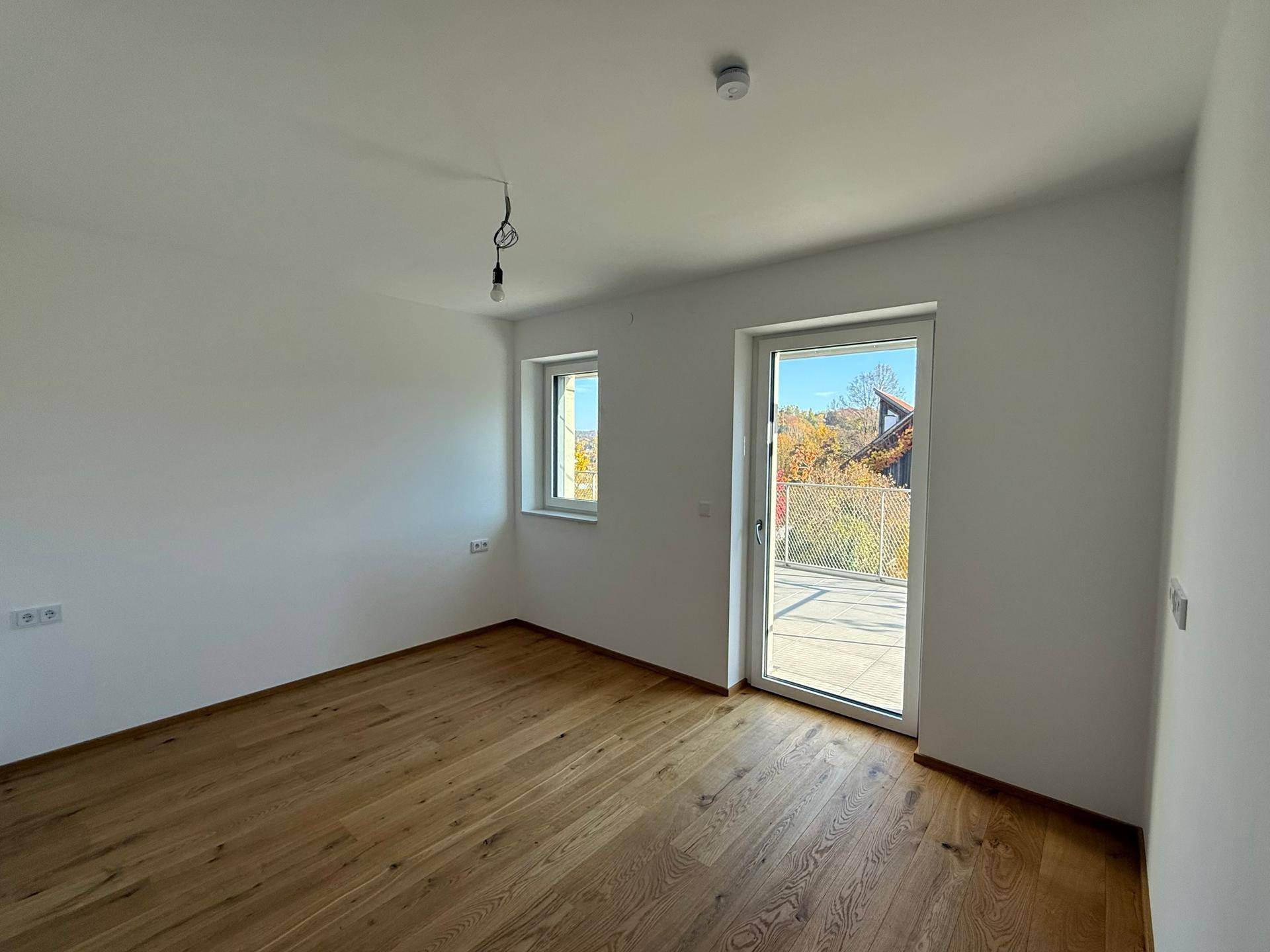 Helles Schlafzimmer mit Holzboden und Fenster mit Zugang zum Außenbereich.