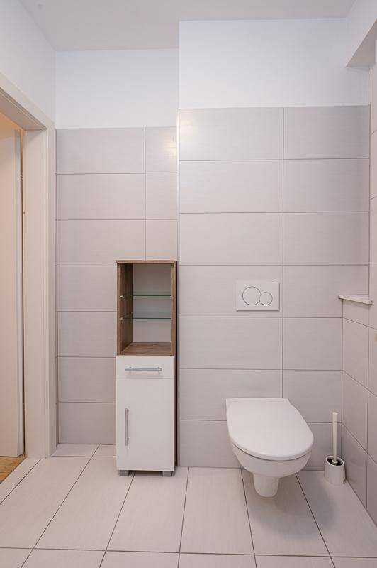Helle Gästetoilette mit wandhängendem WC und einem schmalen Hochschrank für Stauraum.
