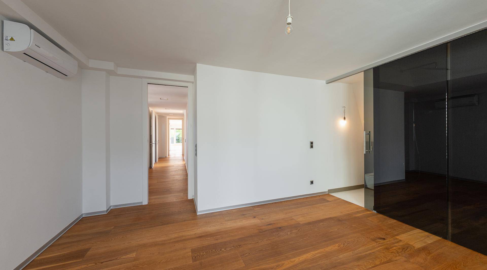 Geräumiger, heller Raum mit Holzboden, Klimaanlage und moderner Glasschiebetür.