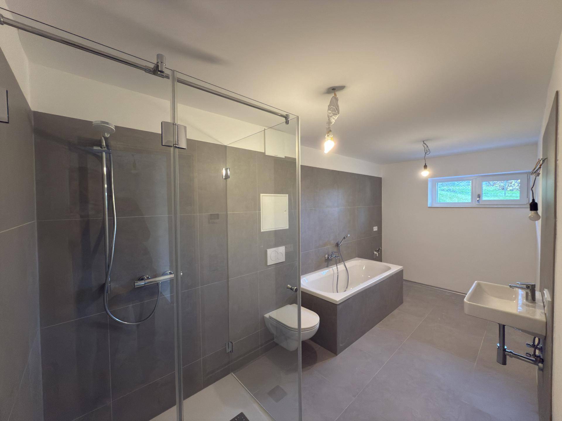 Geräumiges Badezimmer mit Badewanne, Duschkabine, Wand-WC und Einzelwaschbecken.