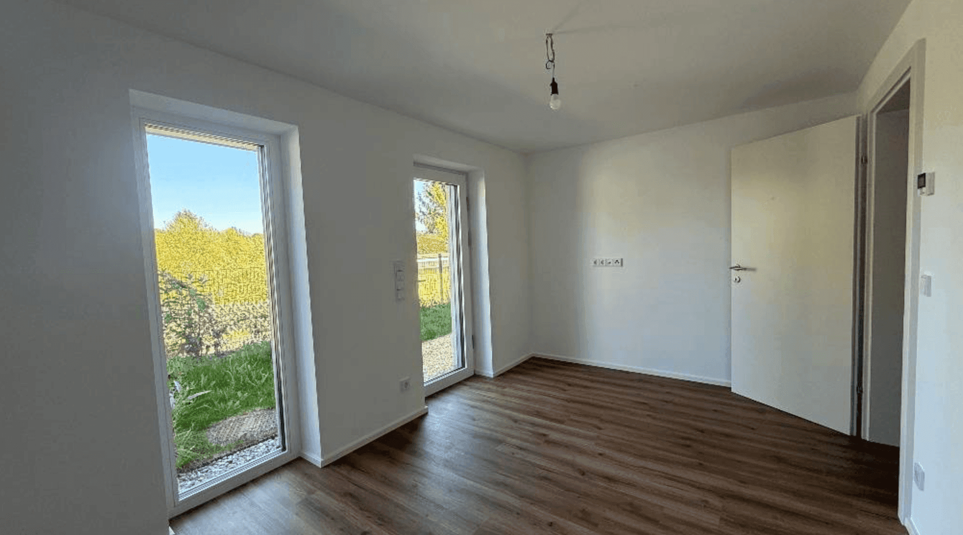 Freundliches Zimmer mit Laminatboden und doppelten Fenstertüren, bietet direkten Zugang zum Garten.