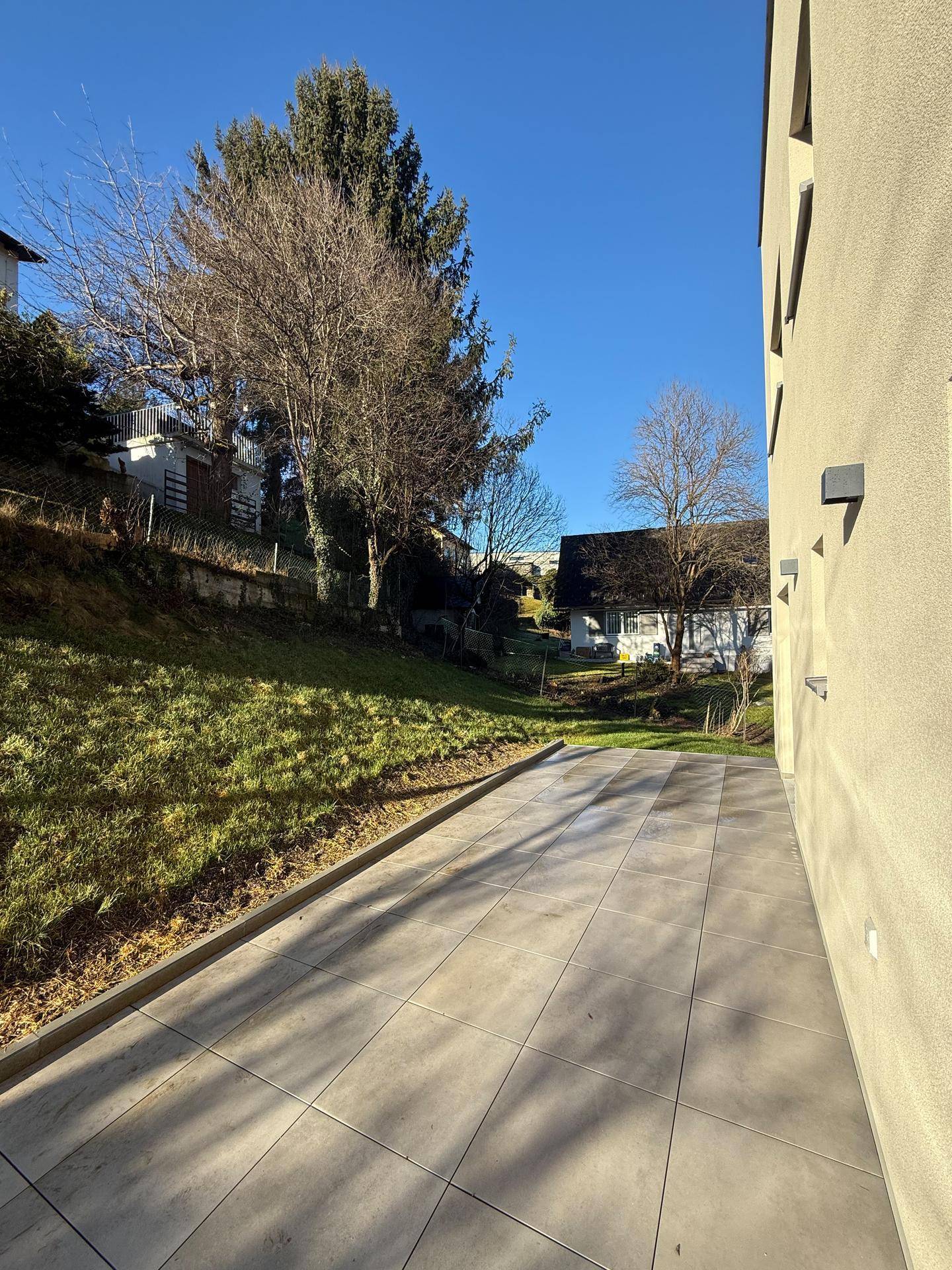 Große, geflieste Terrasse entlang des Gebäudes mit Zugang zum Gartenbereich.