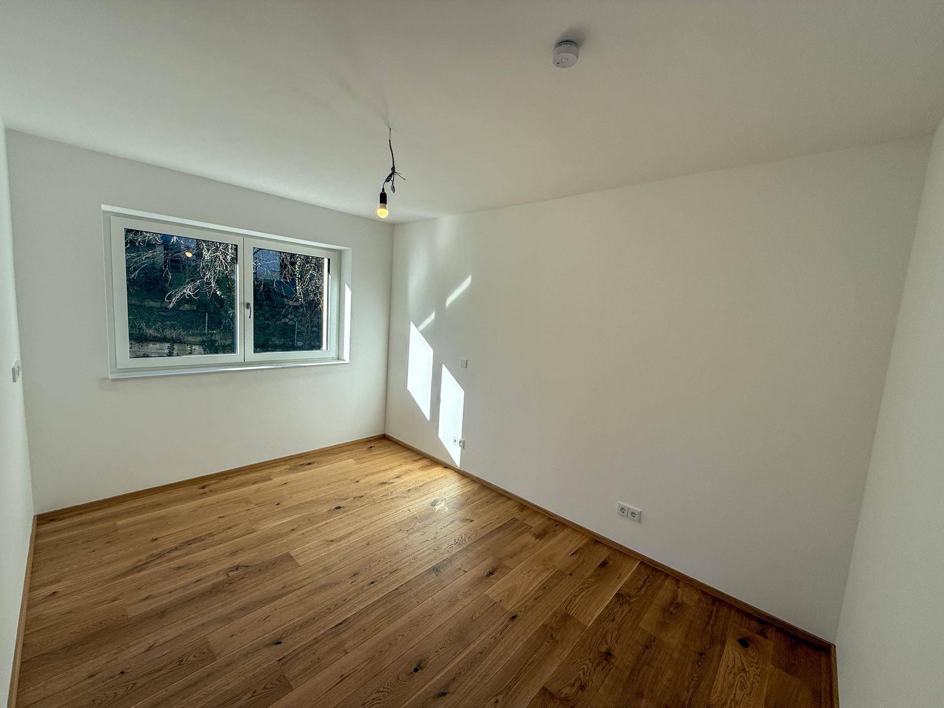 Helles Schlafzimmer mit Holzboden und Fenster, das viel Tageslicht hereinlässt.