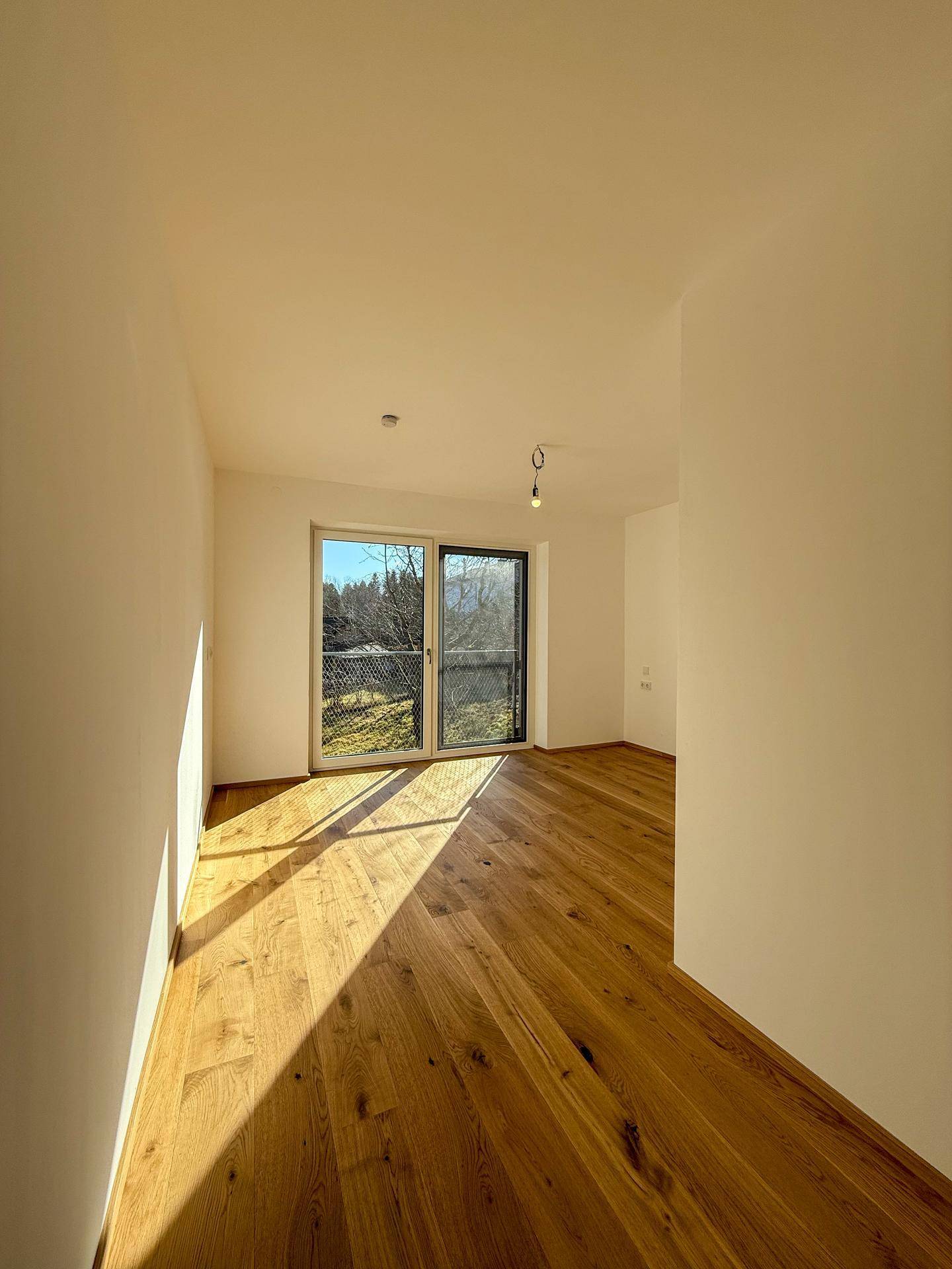 Helles Schlafzimmer mit Holzboden und großem Fenster mit Zugang zum Außenbereich.
