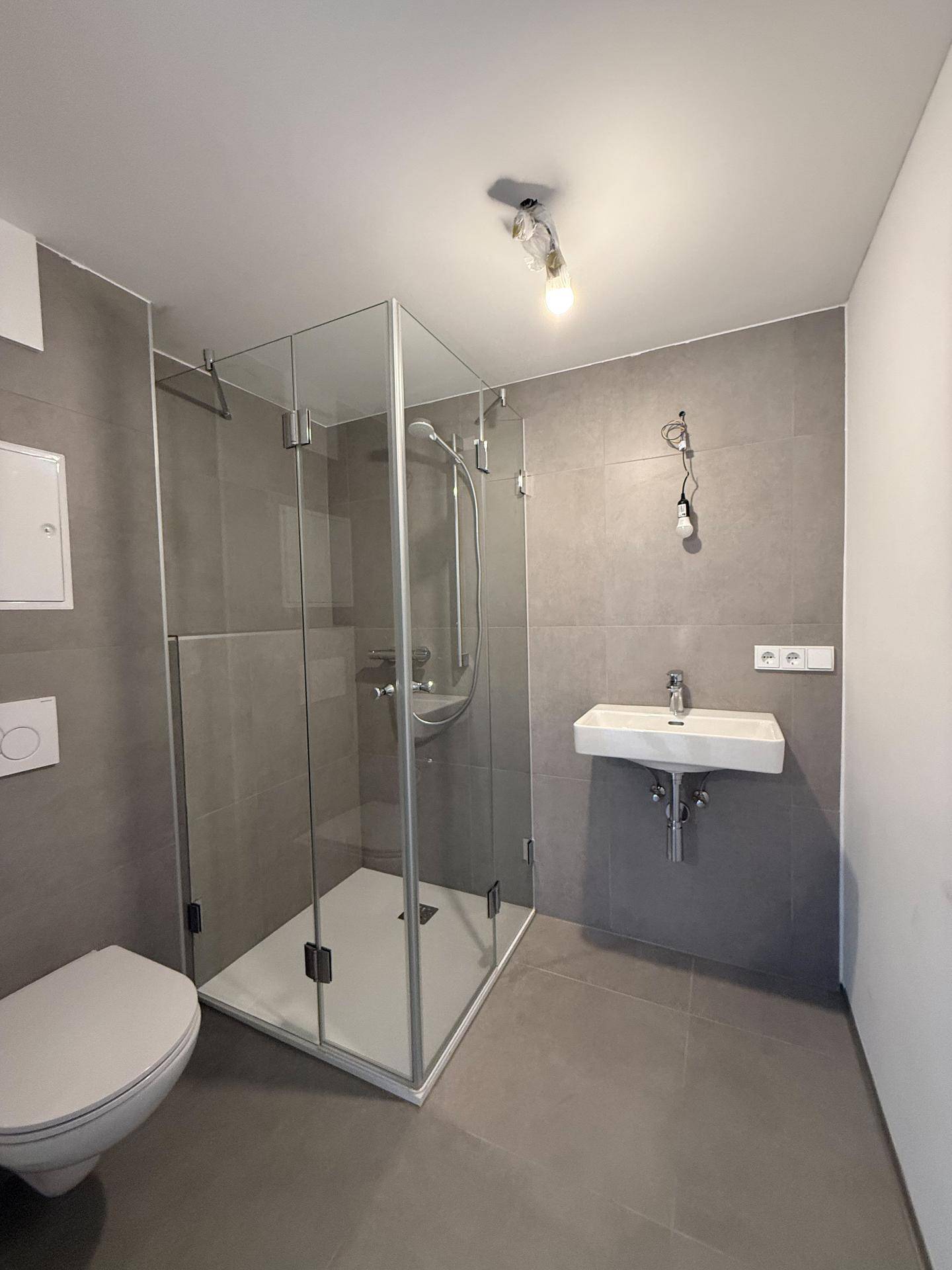 Zeitgemäßes Badezimmer mit Glasduschkabine, Wand-WC und Einzelwaschbecken.