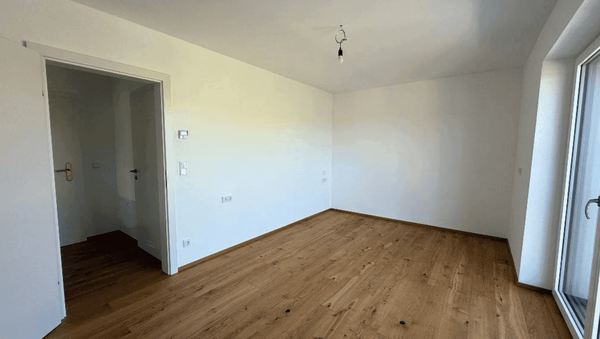 Geräumiges Schlafzimmer mit Holzboden und großen Fenstern, die den Raum mit natürlichem Licht füllen.