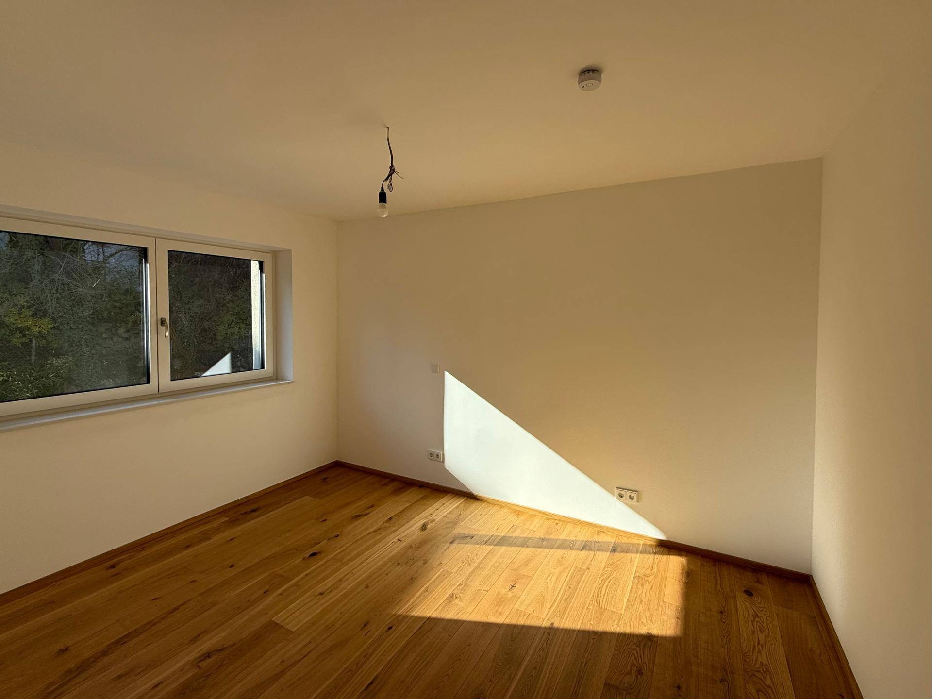 Helles Schlafzimmer mit Holzboden und Fenster, das viel Tageslicht hereinlässt.