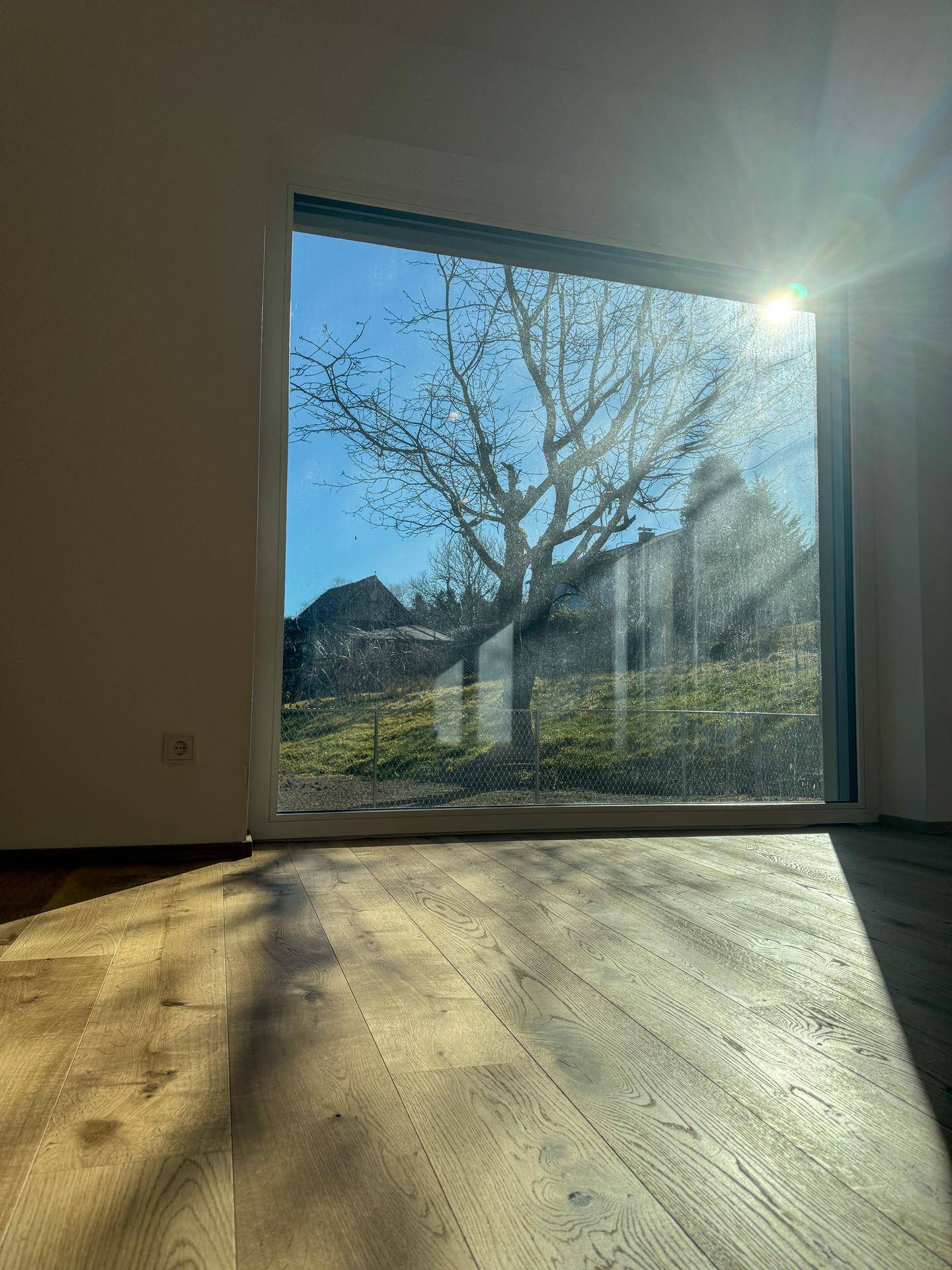 Großes Fenster im Wohnbereich mit Blick auf die umliegende Landschaft und viel Sonnenschein.