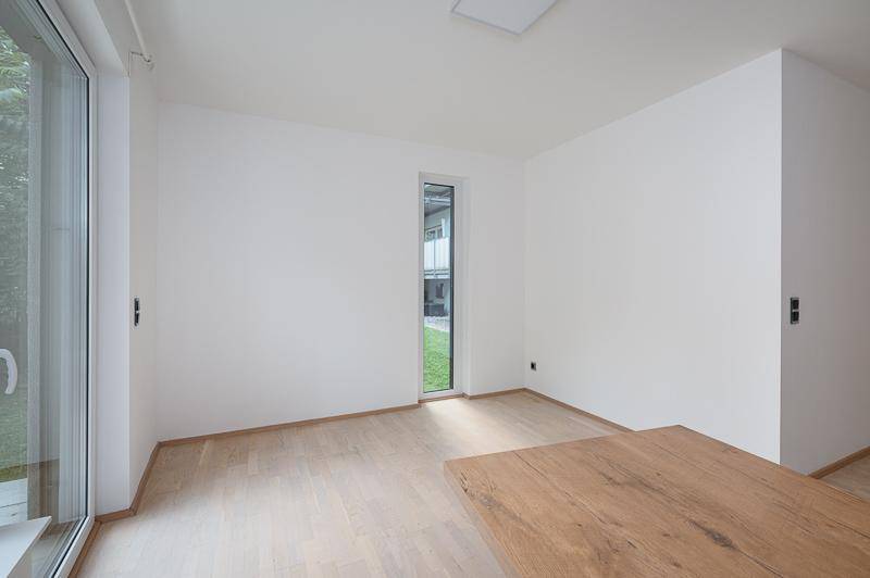 Heller, leerer Raum mit Parkettboden und einem hohen, schmalen Fenster.