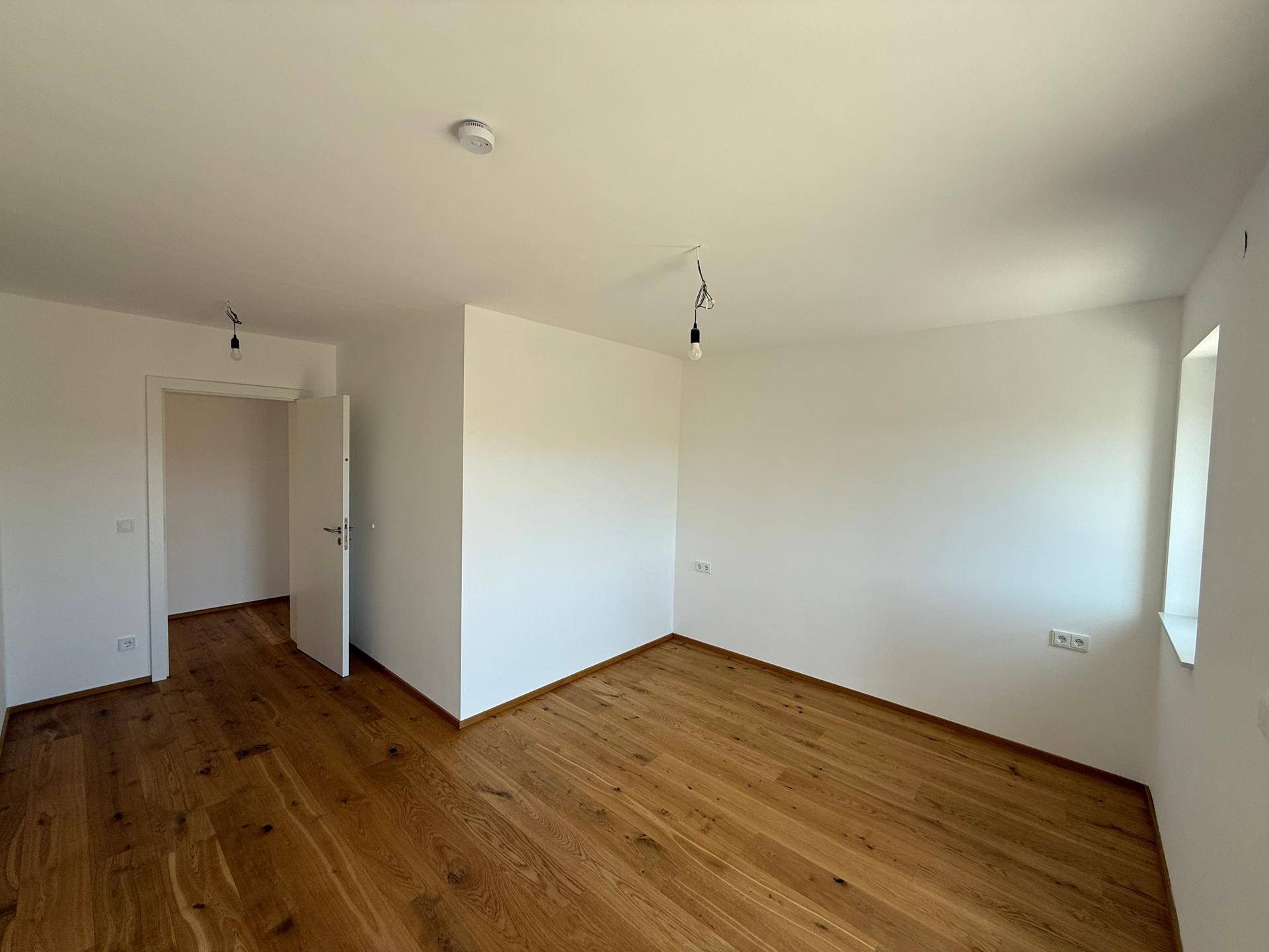 Helles Schlafzimmer mit Holzboden und Fenster, das viel Tageslicht hereinlässt.