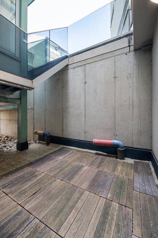 Kleiner Außenbereich mit Holzplankenboden und Betonwänden, umgeben von moderner Architektur.