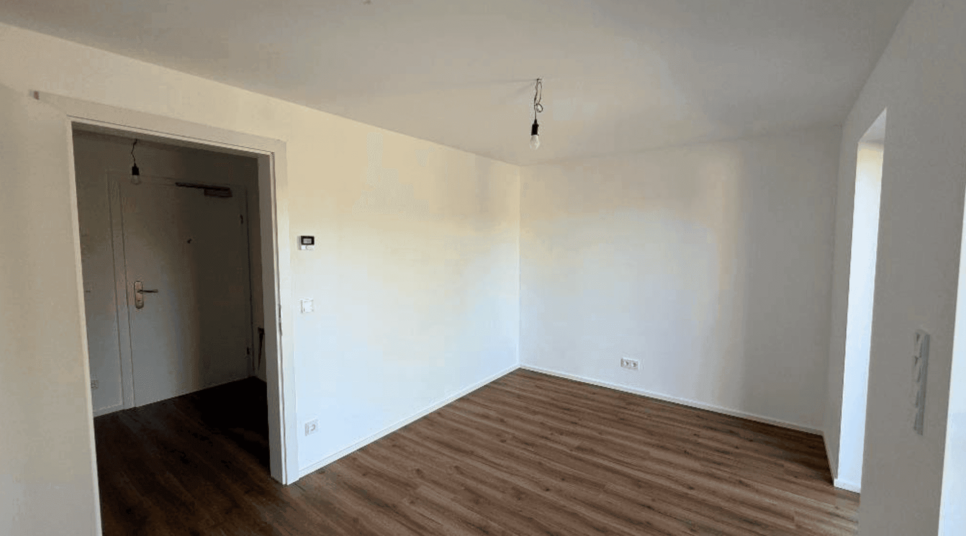 Schlichtes Zimmer mit Laminatboden und weiß gestrichenen Wänden, bereit für individuelle Einrichtung.