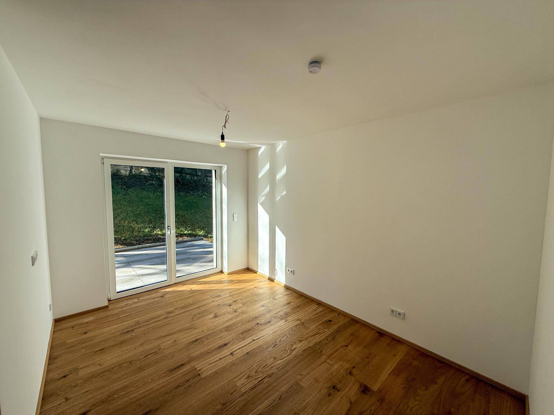 Helles Schlafzimmer mit Holzboden und großem Fenster, das den Raum erhellt.