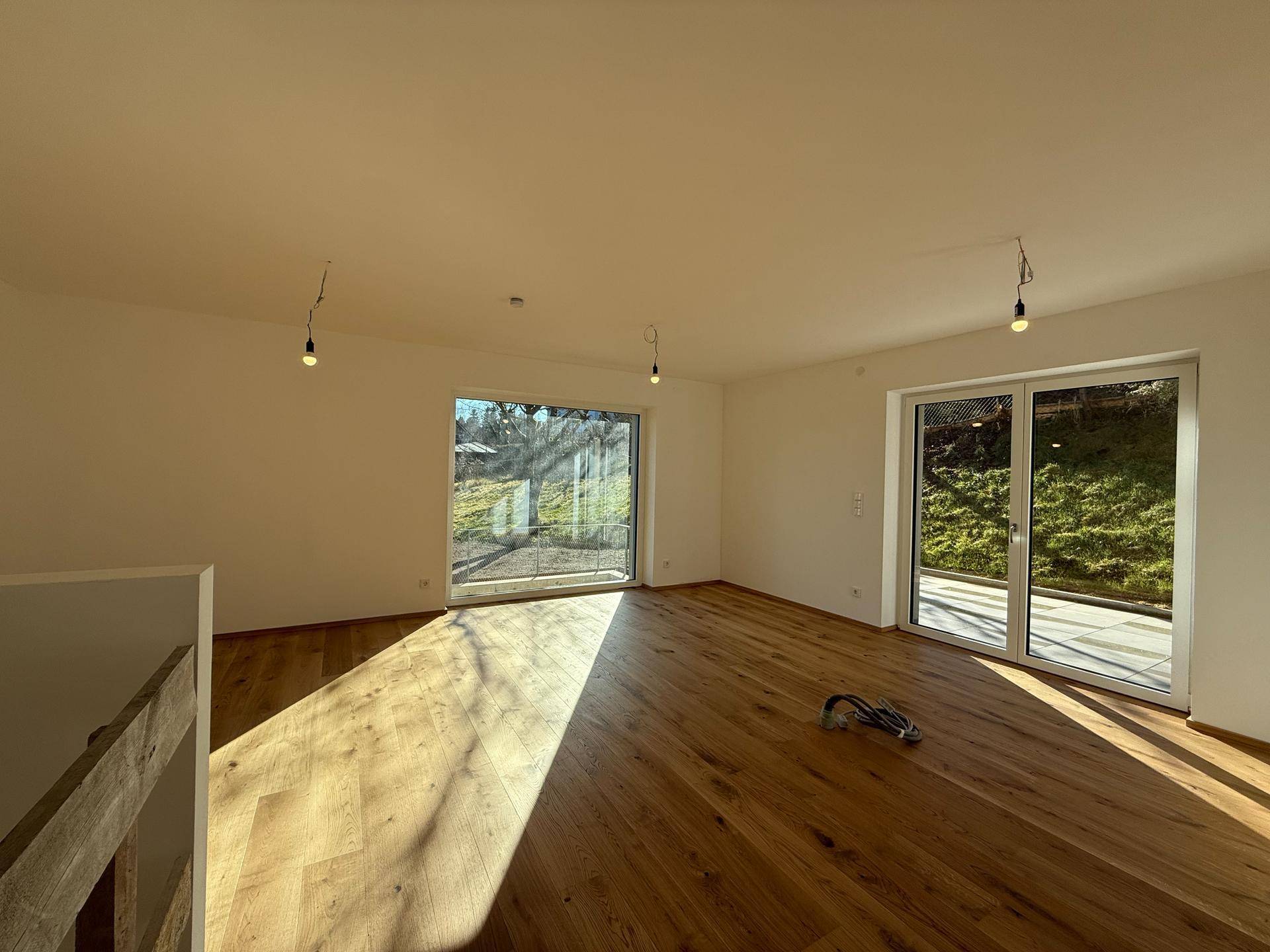 Geräumiger Wohnbereich mit Holzboden und großen Fenstern, die viel Licht spenden.