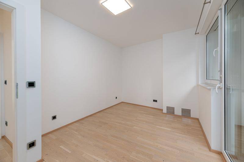 Heller, leerer Raum mit Parkettboden und großem Fenster, das viel Tageslicht hereinlässt.