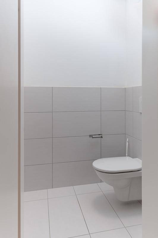 Helle Gästetoilette mit wandhängendem WC und weißen Fliesen an den Wänden und am Boden.