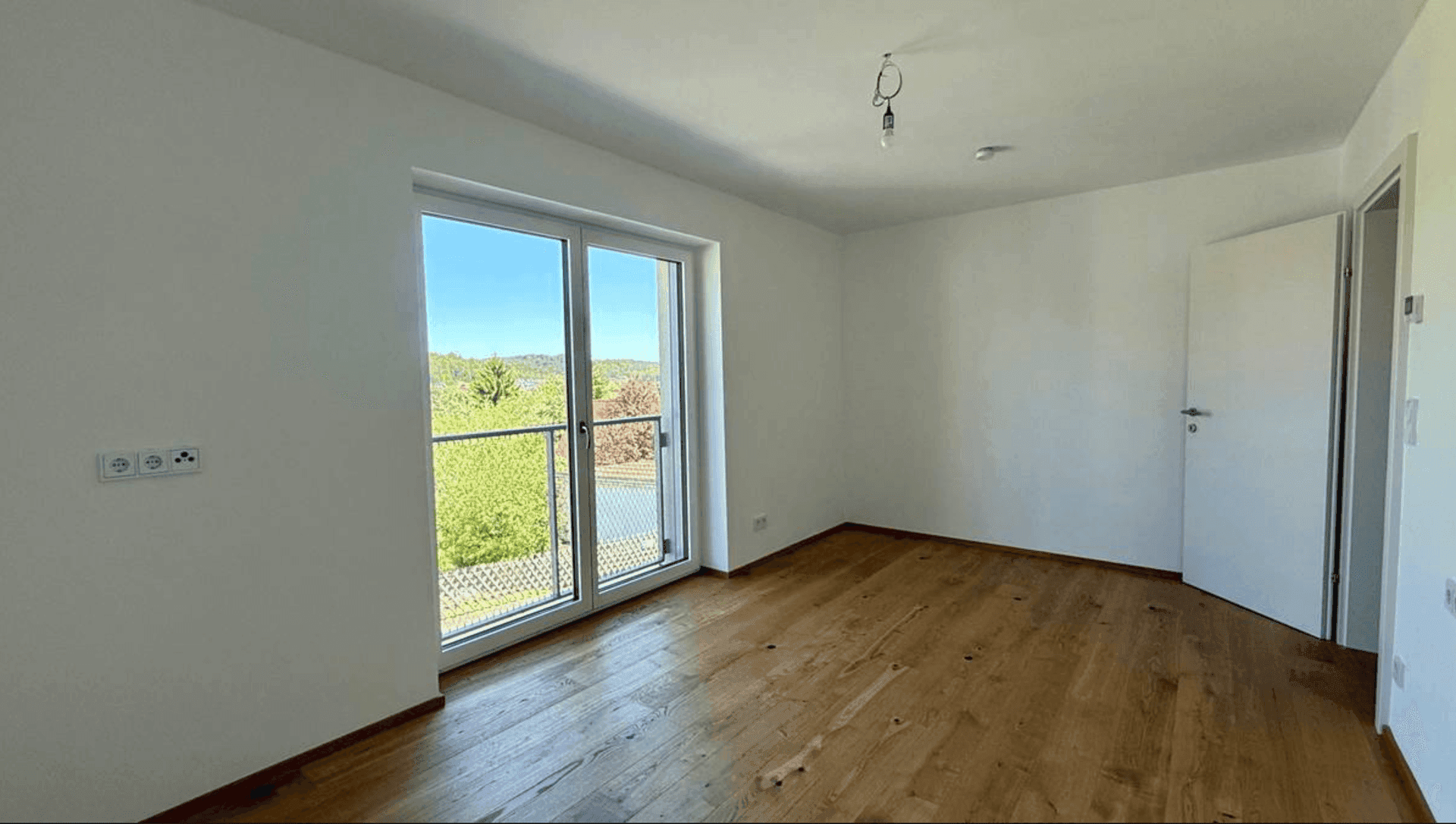 Helles Schlafzimmer mit Holzboden und Zugang zu einem Balkon, bietet viel Tageslicht und frische Luft.