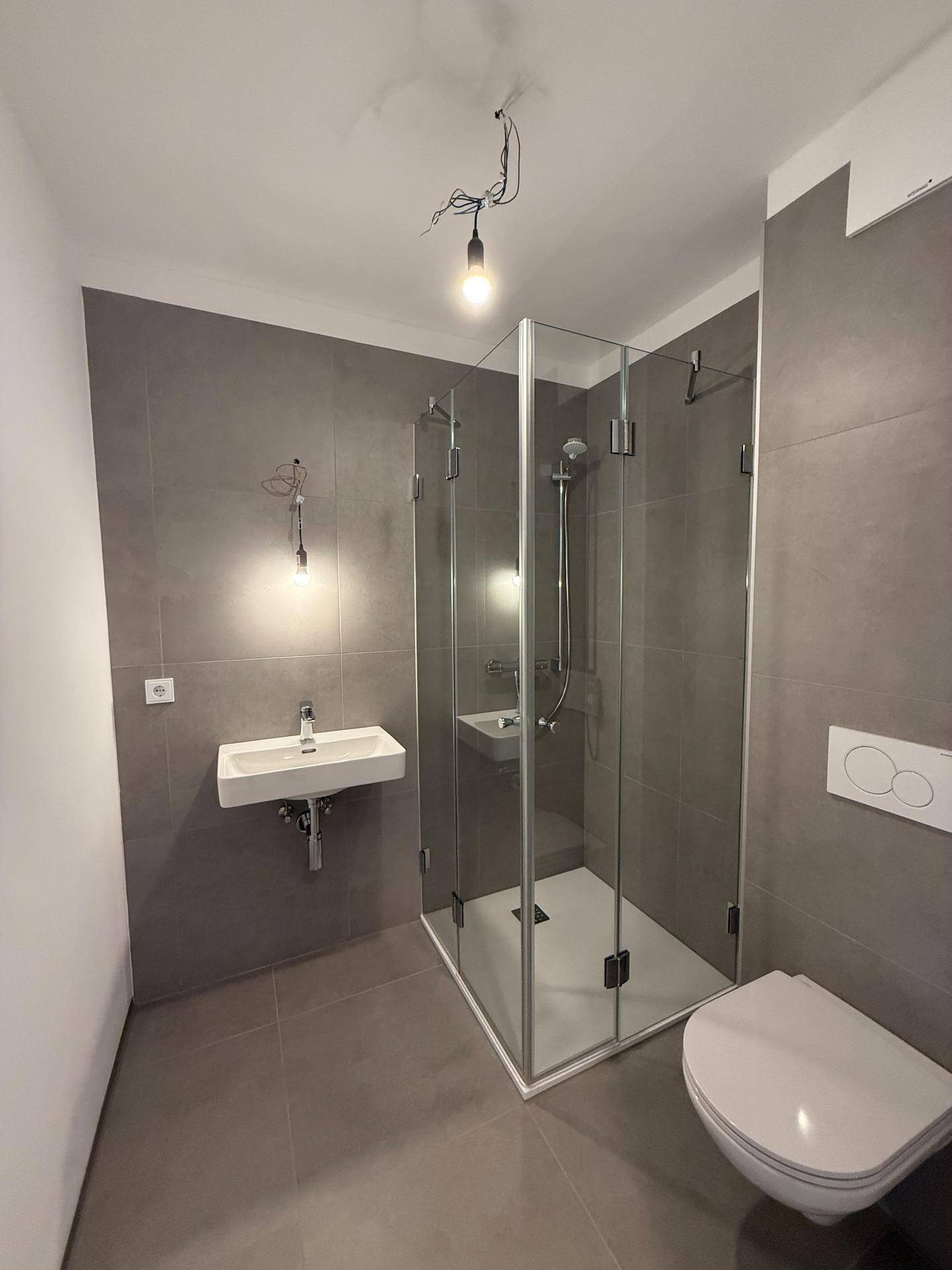 Modernes Badezimmer mit Duschkabine, Wand-WC, Einzelwaschbecken und Fliesenboden.