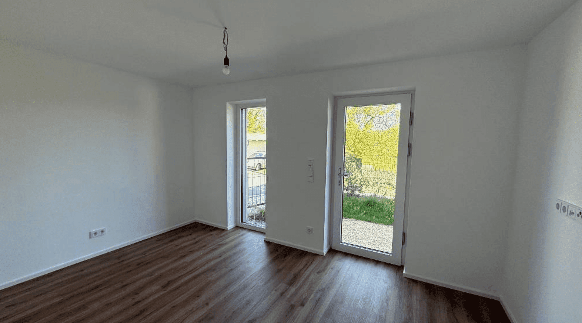 Helles Zimmer mit Laminatboden und zwei Fenstertüren, die Zugang zum Außenbereich ermöglichen.