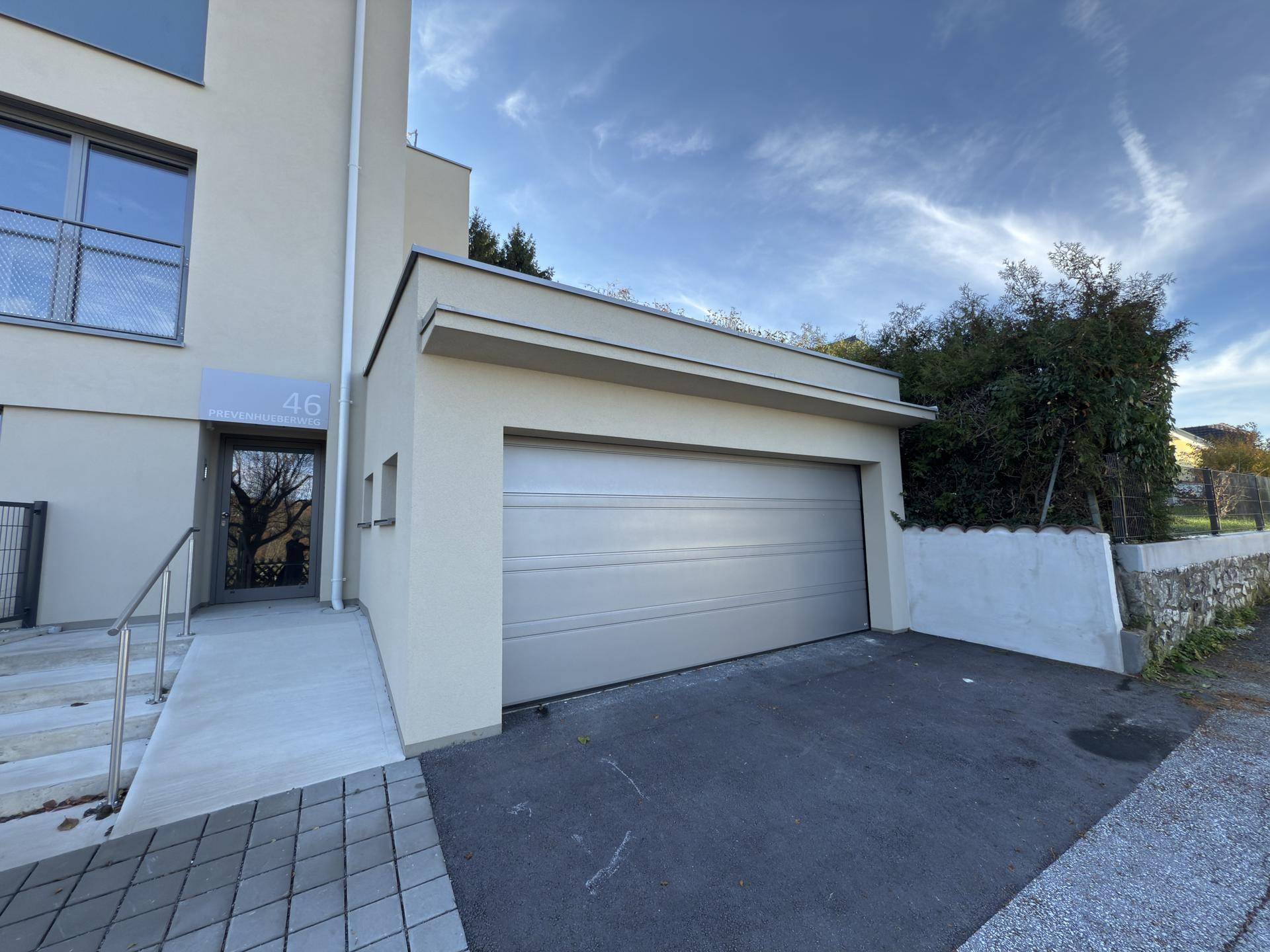 Moderne Gebäudefassade mit integrierter Garage und gepflegtem Eingangsbereich.