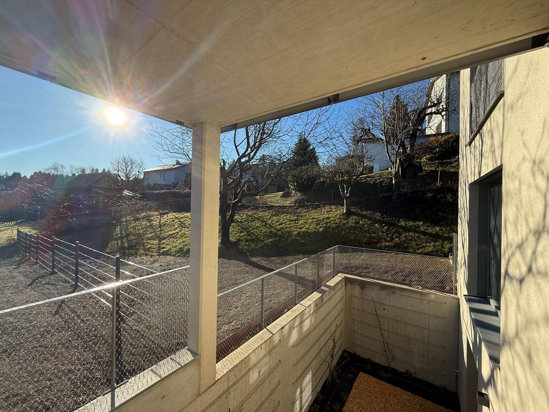 Überdachter Balkon mit Blick auf die grüne Umgebung und viel Sonnenschein.