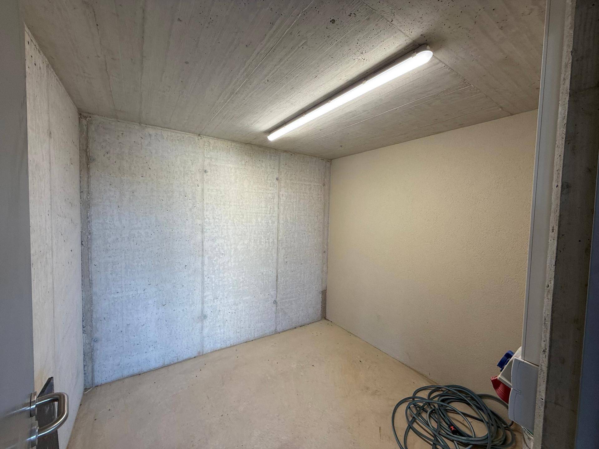 Praktischer Abstellraum mit Betonwänden und einfacher Beleuchtung für zusätzlichen Stauraum.