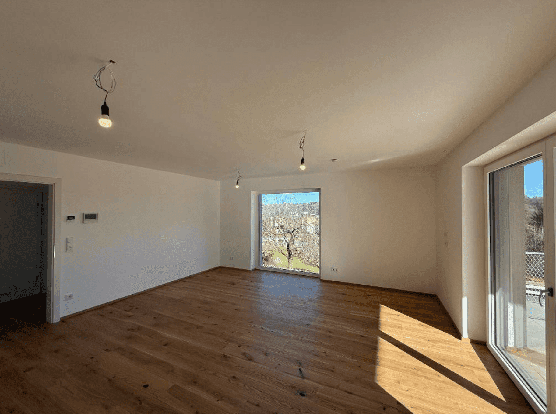 Modernes Wohnzimmer mit Holzboden und großem Fenster, das viel Tageslicht und eine schöne Aussicht bietet.