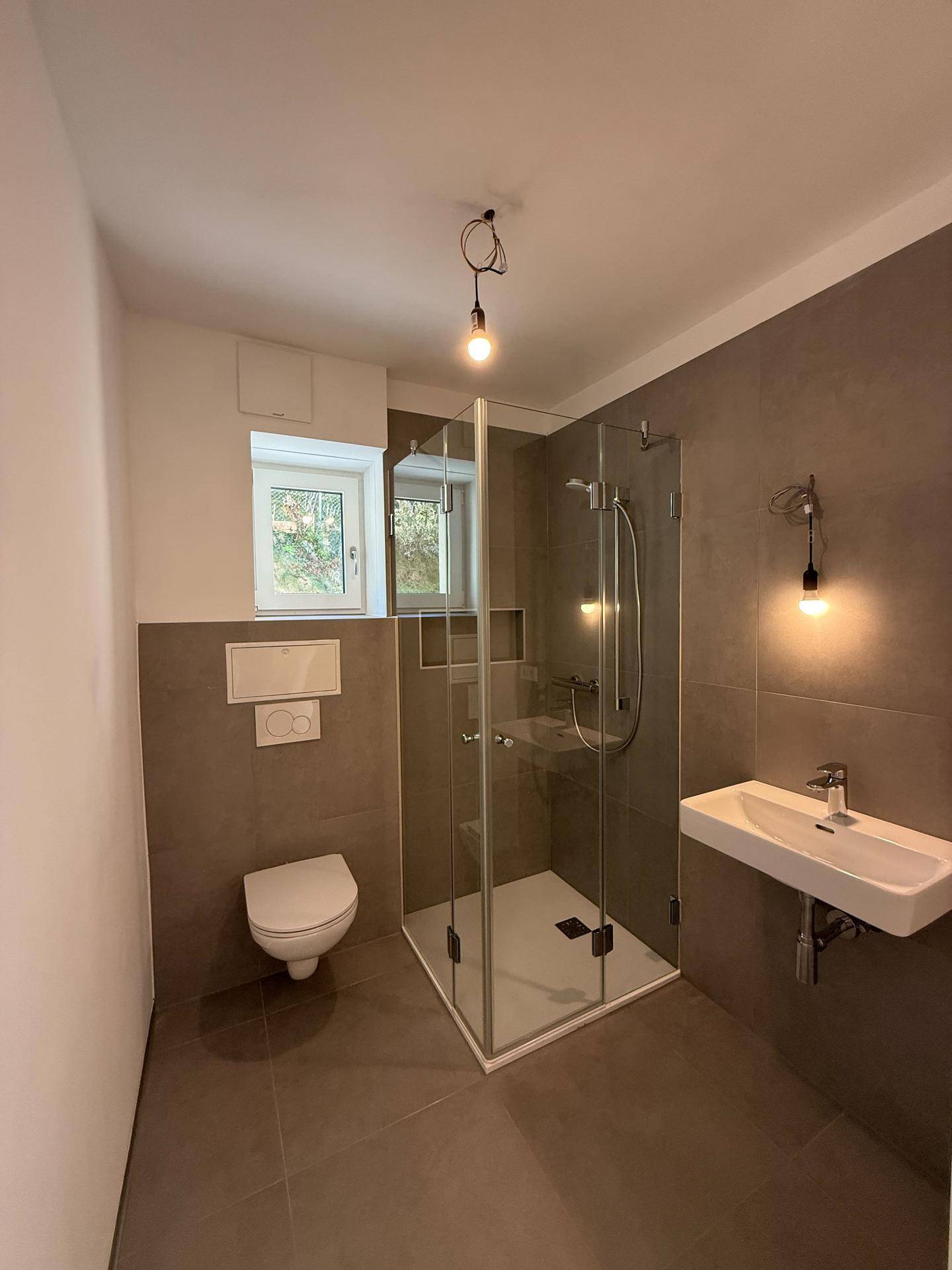 Modernes Badezimmer mit Duschkabine, Wand-WC, Einzelwaschbecken und Fenster.