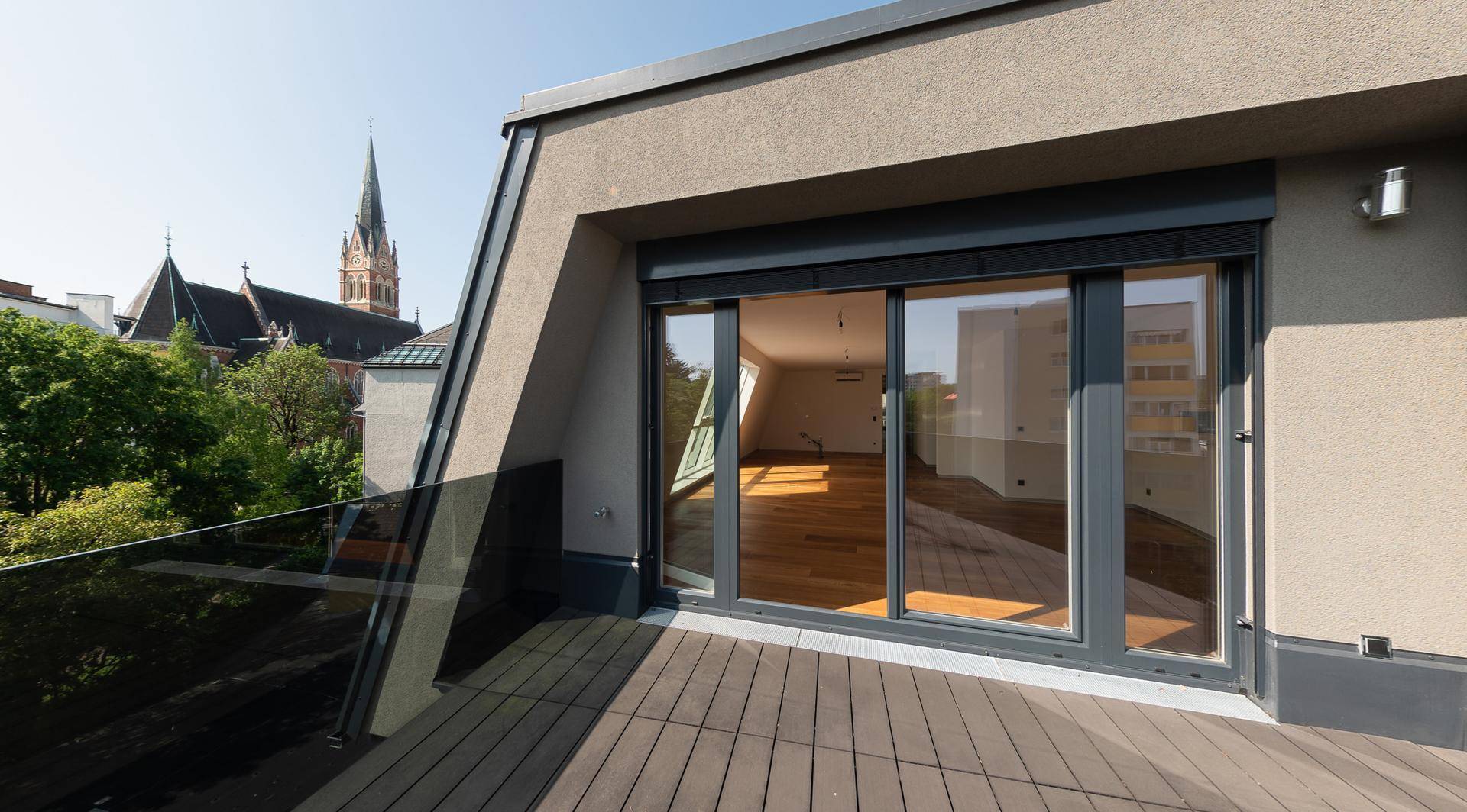 Moderne Terrasse mit Holzboden und Glasgeländer, bietet Blick auf eine Kirche und die Stadt.