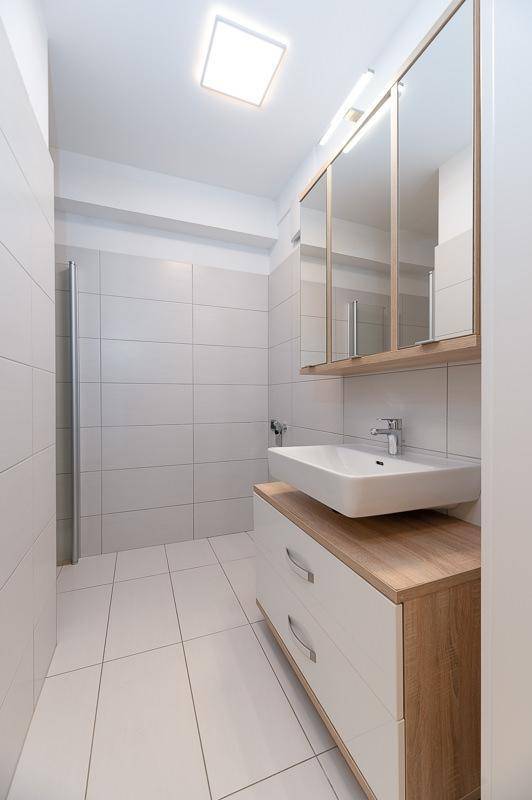Modernes Badezimmer mit weißem Waschbecken auf Holzunterschrank und großem Spiegelschrank.