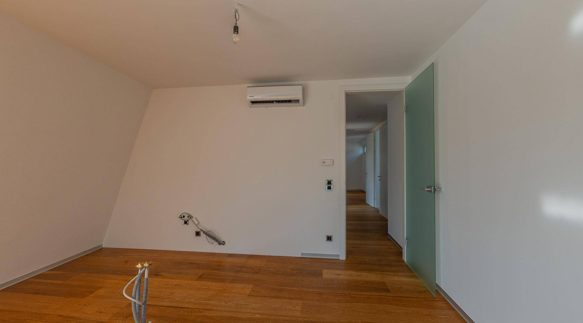Innenraum mit Holzboden, Klimaanlage und einer modernen Glastür zum Flur.